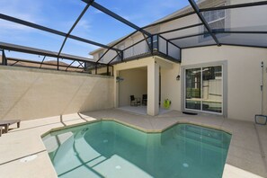 A swimming pool with a covered patio area, a door leading to a covered porch, and a hose on the wall. - Championsgate Pool Home Near Disney Parks (Davenport)