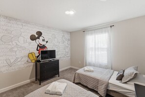 A bedroom with two beds, a TV on a dresser, and a Mickey Mouse mural on the wall. - Championsgate Pool Home Near Disney Parks (Davenport)