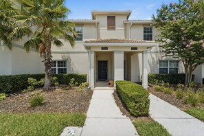 A two-story building with a covered entrance and numbered doors, surrounded by well-maintained landscaping. - Championsgate Pool Home Near Disney Parks (Davenport)