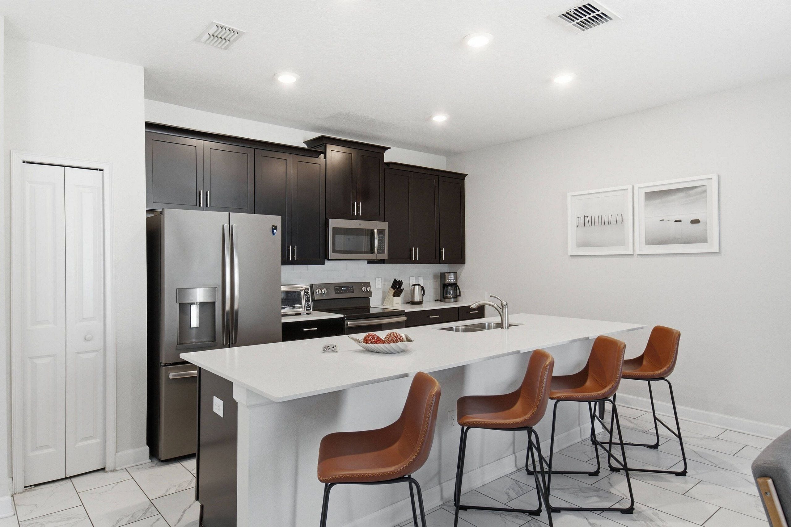 Una cocina moderna con armarios oscuros, electrodomésticos de acero inoxidable, una isla central con taburetes de bar y una encimera blanca.