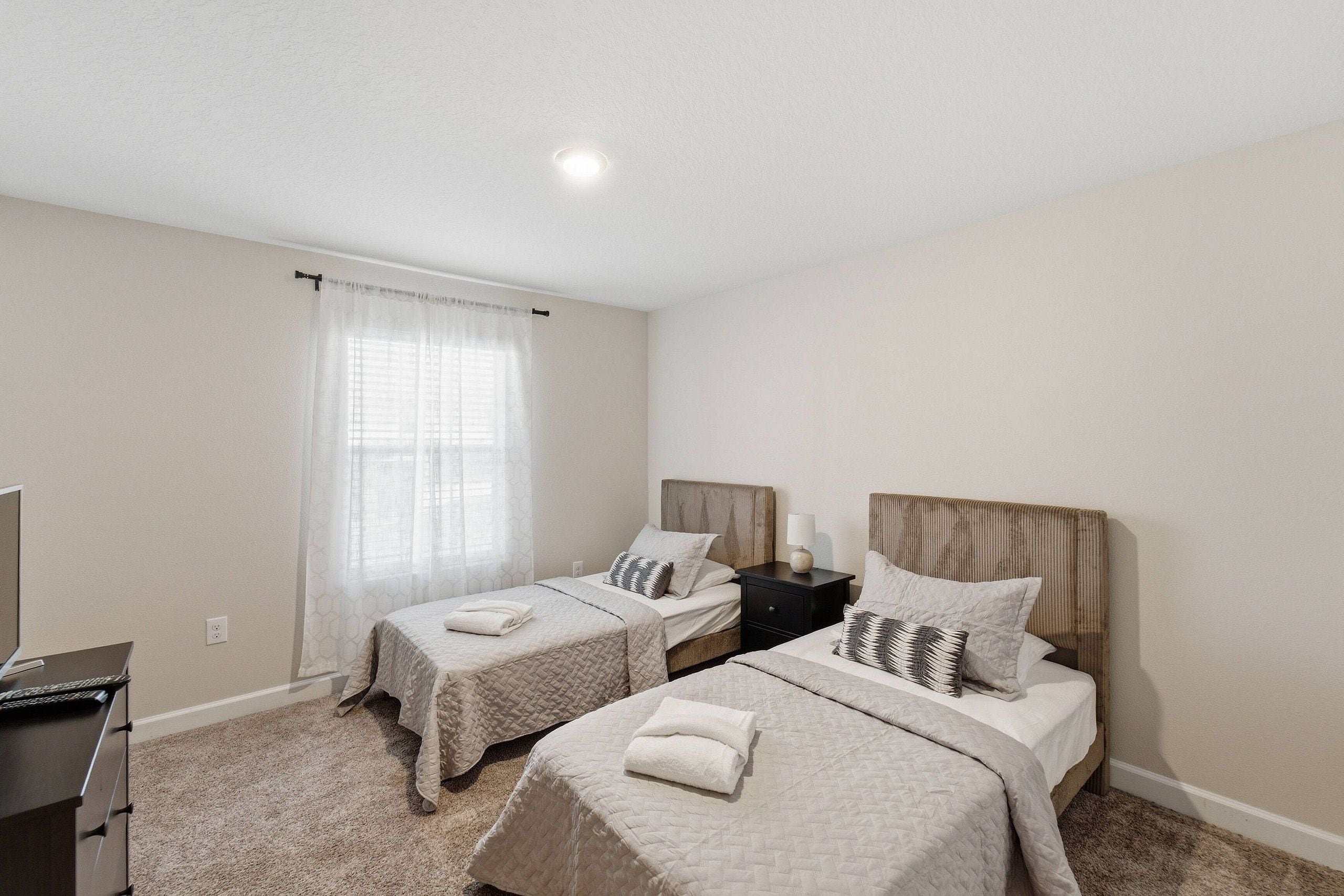 A hotel room with two single beds, a desk, and a television.