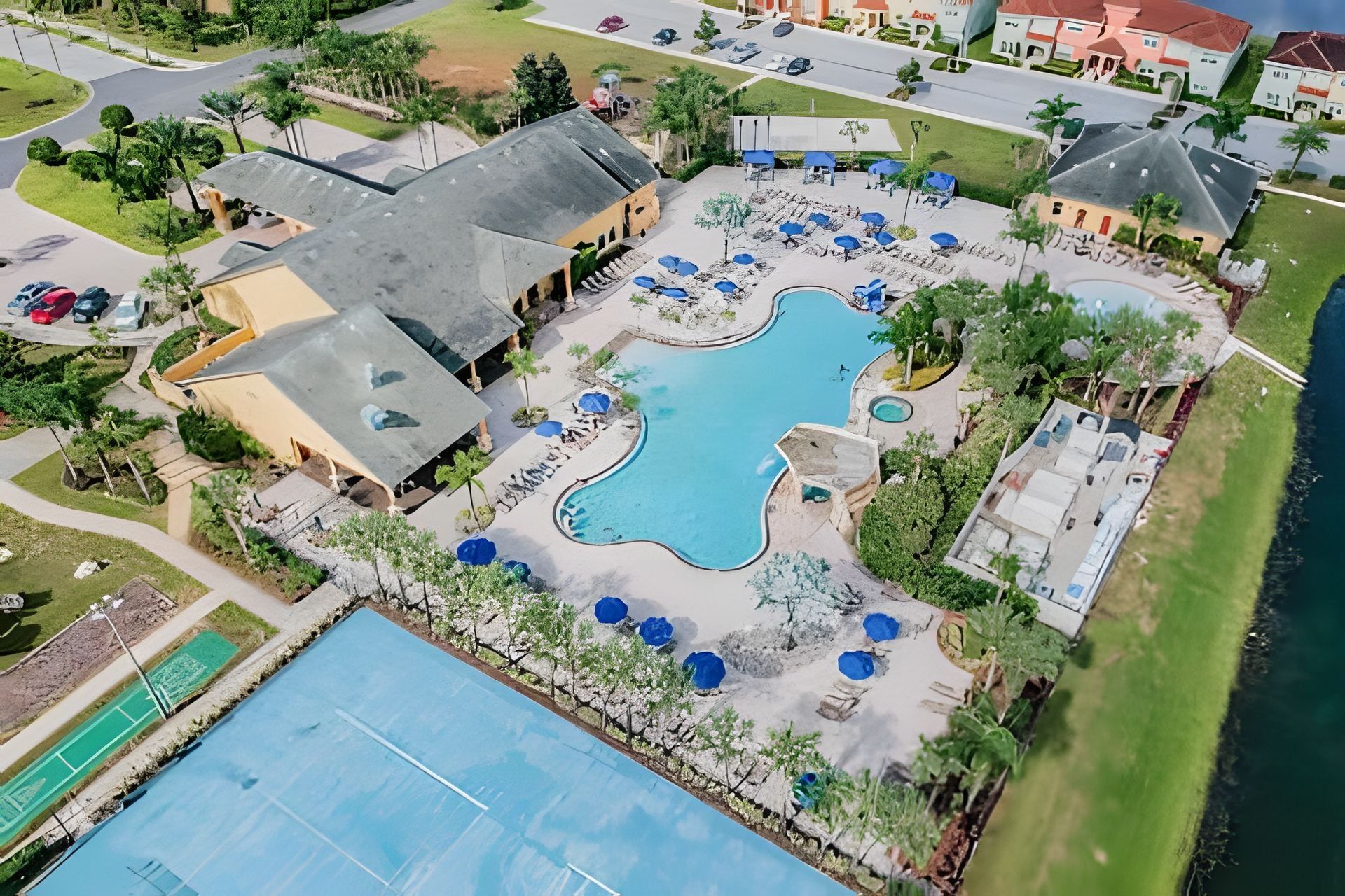 An aerial view of a resort with a large pool, tennis courts, and multiple buildings with roofs.