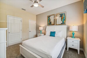 A bedroom with a bed, two nightstands, a ceiling fan, and two wall-mounted paintings. - 4BR Paradise Palms Townhome, Heated Pool (Kissimmee)