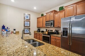 A kitchen with granite countertops, stainless steel appliances, wooden cabinets, and a built-in microwave. - 4BR Paradise Palms Townhome, Heated Pool (Kissimmee)