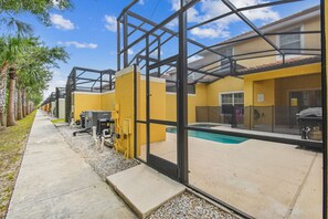 A modern building with a glass facade, a swimming pool, and a concrete pathway lined with palm trees. - 4BR Paradise Palms Townhome, Heated Pool (Kissimmee)
