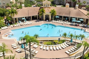 A large swimming pool surrounded by lounge chairs and umbrellas, with palm trees and a building in the background. - Vista Cay 3BR Townhome Near Universal & Occc (Orlando)