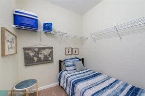 A bedroom with a bed, a shelf with storage bins, a fan, a world map, and a framed picture. - Stylish 3BR Apartment at Vista Cay Resort (Orlando)