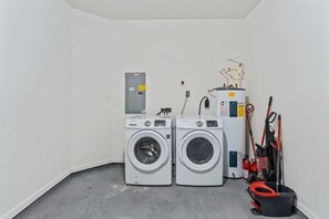 A laundry room with two front-loading washing machines, a water heater, and cleaning tools. - Modern 3BR Condo With Balcony at Vista Cay (Orlando)