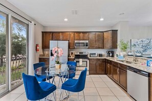 Une cuisine moderne avec une table à manger en verre, des chaises bleues et des meubles de rangement en bois.