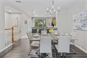 A modern dining area with a glass table, white chairs, and a chandelier. - Modern 3BR Condo With Balcony at Vista Cay (Orlando)