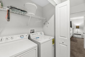 A laundry room with two white washers and dryers, a drying rack, and a small cabinet. - 4BR Home Storey Lake Resort w/ Pool (Kissimmee)