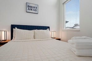 A bedroom with a bed, two bedside lamps, a window with blinds, and a sign on the wall. - Modern Waterfront Escape on Lake Buchanan (Buchanan Dam)