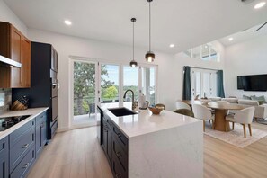 A modern kitchen with a central island, a dining area with a round table, and a living room with a flat-screen TV. - Modern Waterfront Escape on Lake Buchanan (Buchanan Dam)