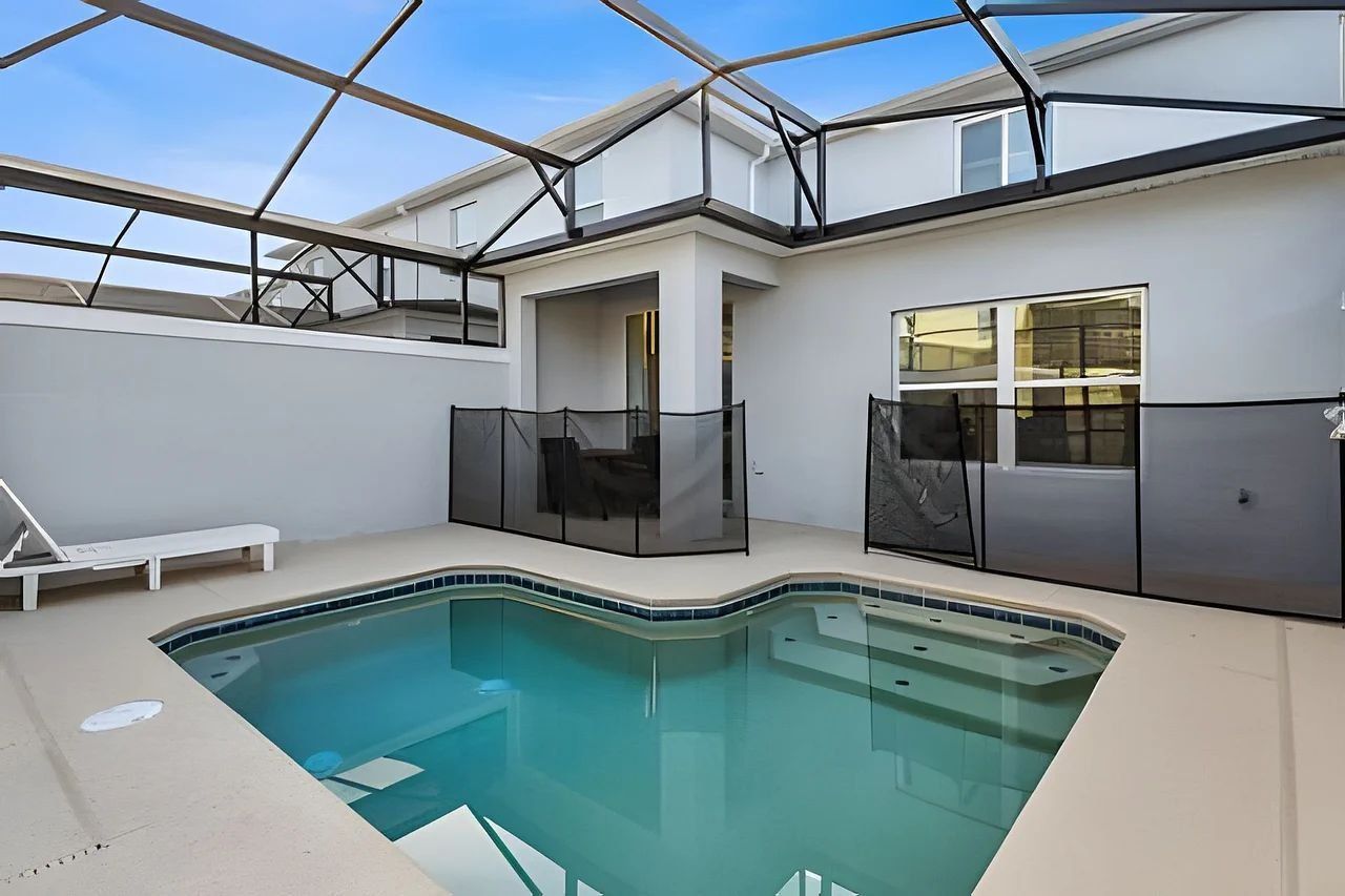 A swimming pool with a glass enclosure, a lounge chair, and a modern building with large windows.