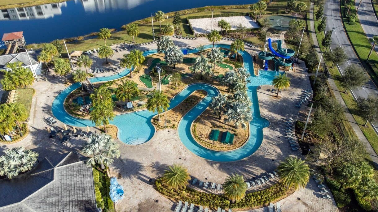 Luchtbeeld van een resort met meerdere zwembaden, palmbomen en een glijbaan.