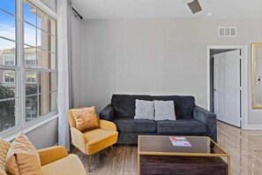 A living room with a dark grey sofa, a yellow armchair, and a glass coffee table. - Modern 3BR Condo at Vista Cay Near Disney (Orlando)