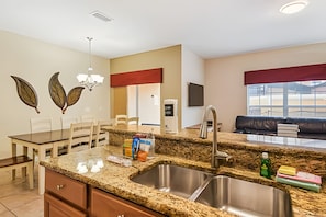 A modern kitchen with granite countertops, a stainless steel sink, and a dining area with a table and chairs. - 4BR Paradise Palms Townhome With Pool (Kissimmee)