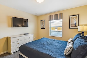 A bedroom with a bed, dresser, TV, window, and artwork. - 4BR Paradise Palms Townhome With Pool (Kissimmee)