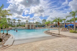 A large outdoor swimming pool with a paved walkway, surrounded by palm trees and a stone structure. - 4BR Paradise Palms Townhome With Pool (Kissimmee)