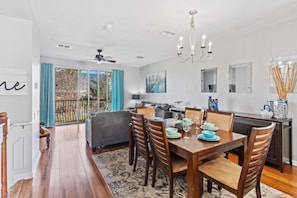 A modern dining area with a wooden table set for four, a ceiling fan, and a view through a glass door to the outdoors. - 3-bedroom Condo at Vista Cay Near Disney (Orlando)