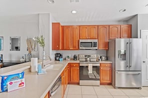A modern kitchen with wooden cabinets, stainless steel appliances, and a large island with a sink. - 3-bedroom Condo at Vista Cay Near Disney (Orlando)