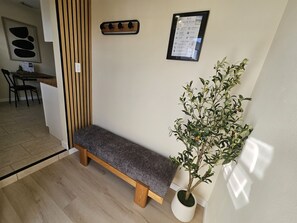 Een bank, een muurhaak voor jassen, een bord met huisregels in een lijst en een potplant in de hoek.