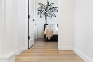A hallway with a wooden floor leading to a bedroom with a bed. - Sunset View Updated Villa Heated Pool  Kings (Waikoloa Village)
