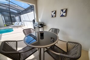Une table ronde avec quatre chaises, un barbecue et deux œuvres d’art murales.
