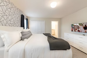 A modern bedroom with a large bed, a white dresser, a flat-screen TV, and a geometric wall design. - 4BR Storey Lake Townhome w/ Private Pool (Kissimmee)
