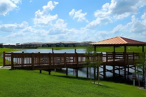 Eine Holzterrasse über dem Wasser mit einem Gartenpavillon, grünem Rasen und Gebäuden in der Ferne.