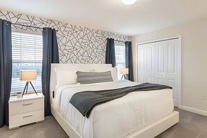Ein modernes Schlafzimmer mit einem weißen Bett, dunklen Vorhängen, einem geometrischen Wanddesign und einer weißen Tür.