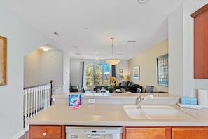 A modern kitchen with a dishwasher, a double sink, and a dining area with a sofa and table. - Spacious 3BR Townhome at Vista Cay Resort (Orlando)