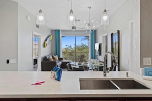A modern kitchen with a central island, a dining area with a table and chairs, and a balcony with a view. - Vista Cay 3BR Condo w/ Balcony & Resort Pool (Orlando)