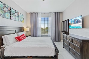 Een hotelkamer met een bed, een televisie, een dressoir en een raam met gordijnen.