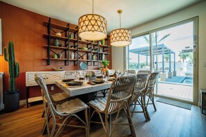 A dining area with a wooden table, wicker chairs, and pendant lights. - Casa Frida | 7BR Spanish Estate w/ Pool, Spa & Cabanas (Coachella)