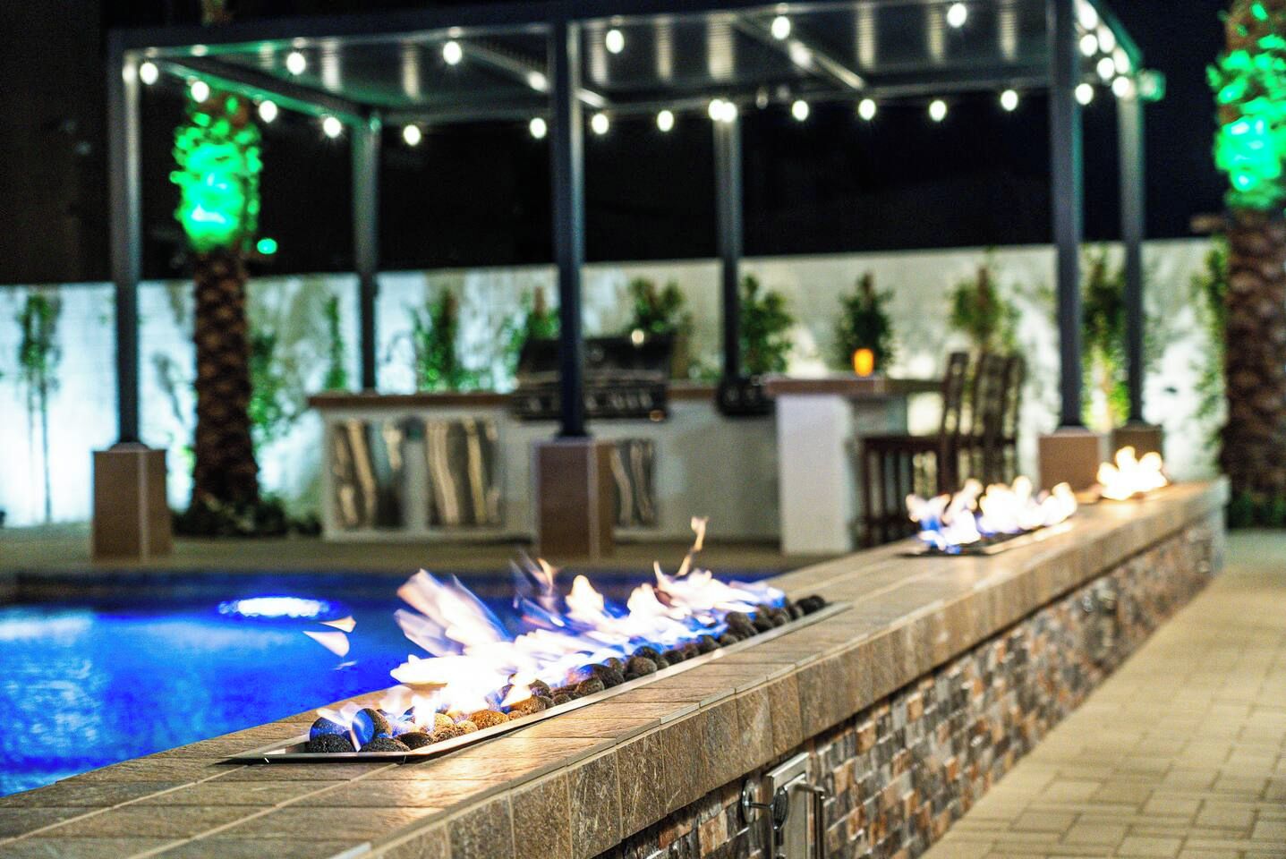 An outdoor pool area with a fire feature, surrounded by a stone wall and potted plants.