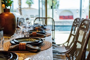 A dining table set with plates, glasses, and cutlery, with a view of the sea in the background. - Casa Frida | 7BR Spanish Estate w/ Pool, Spa & Cabanas (Coachella)