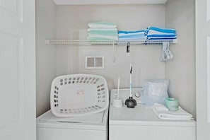A laundry area with a washing machine, a drying rack, a shelf with folded towels, a plug, and a plug adapter. - Modern 3BR Townhome at Vista Cay Resort (Orlando)