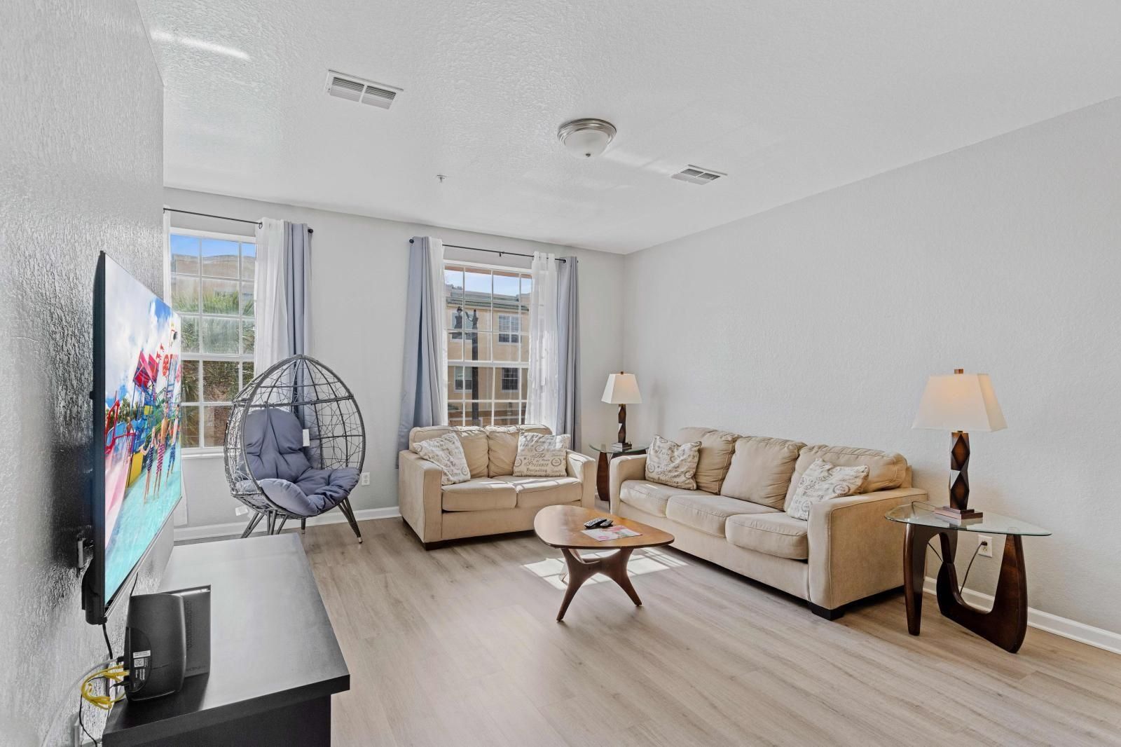 A spacious living room with a large flat-screen TV, a beige sofa, a wooden coffee table, and a hanging chair.