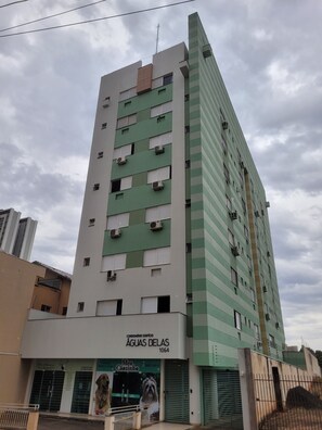 A multi-story building with a green and white facade, multiple air conditioning units, and a visible storefront with a dog advertisement. - Charming loft 850 m from Unicesumar. (Maringá)