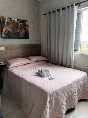 A neatly made bed with a pink bedspread, a pillow, and a folded towel on the bed. - Charming loft 850 m from Unicesumar. (Maringá)