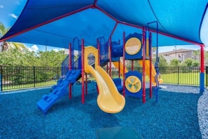 A playground with a slide and climbing structures, surrounded by a blue canopy and a fence. - Spacious 3BR Apartment at Vista Cay Resort (Orlando)