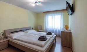 A hotel room with a bed, a desk, a chair, a TV, and a window with curtains. - PRIMAVISTA ZERMATT – PEACEFUL APARTMENT WITH MATTERHORN VIEWS (Zermatt)