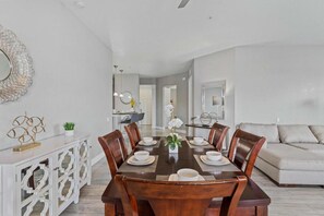 A dining area with a wooden table set for four, surrounded by chairs. A white console with a decorative mirror and a small plant is against the wall. - Spacious 4BR Vista Cay Retreat Near Universal (Orlando)