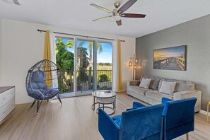 Un salon spacieux avec un balcon, un ventilateur de plafond, un canapé et un fauteuil.