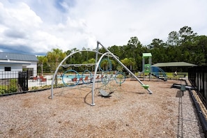 A playground with a swing set, climbing structures, and a slide. - Disney 4BR Townhome w/ Pool Storey Lake (Kissimmee)