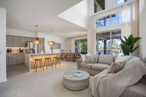 A modern kitchen with a central island, dining area, and a cozy living space with a sofa and ottoman. - Luxury Sunset Villa | Pool Steps Away | 3 Lanais (Waimea)