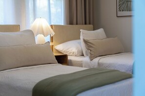 Ein Hotelzimmer mit zwei Betten, einem Nachttisch mit Lampe und einem Fenster mit Vorhängen.