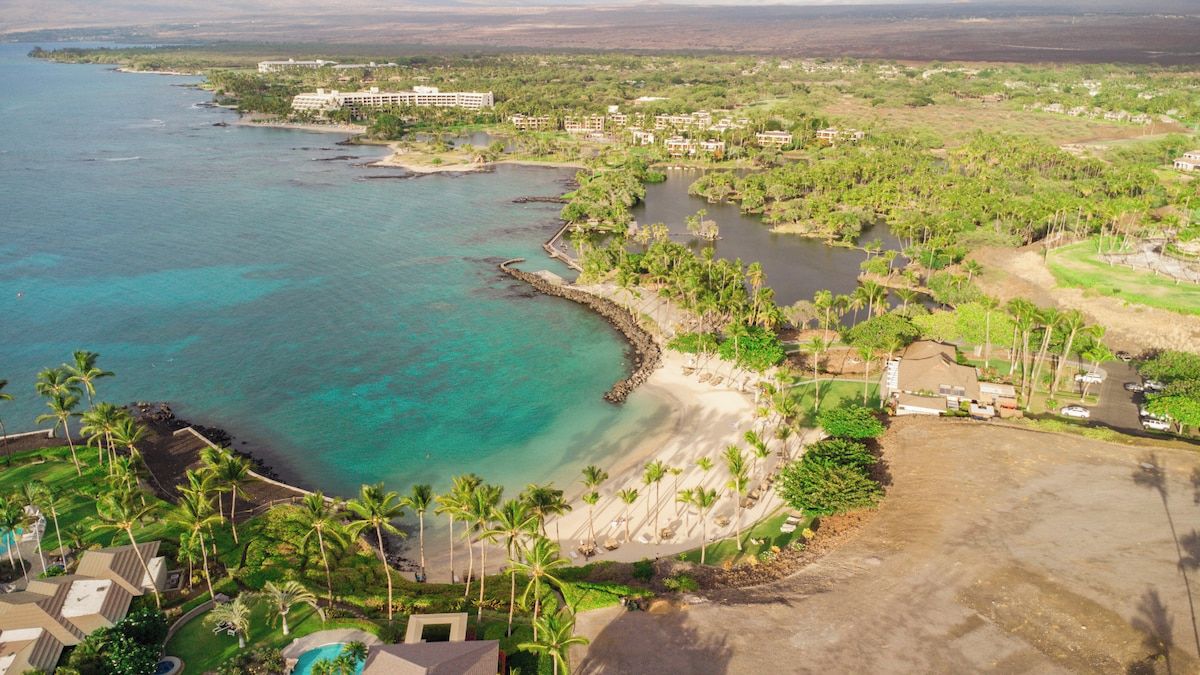 Una località balneare con spiaggia, palme e un grande complesso alberghiero.