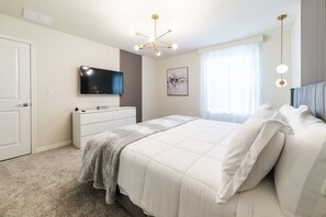 Ein Schlafzimmer mit Bett, Kommode, Fernseher und einem Fenster mit Vorhängen.
